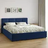 A blue upholstered bed with a botanical print duvet and pillows, set against a white wall with three framed botanical prints above it. A beige curtain is visible on the right. Produktbild-Vorschau