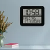 A digital clock is mounted on a light blue wall, displaying the time, day of the week, and date. To the left, a vase with dried flowers and a decorative horse figurine are visible on a white surface, along with two books. Náhled obrázku produktu