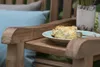 A slice of cake on a plate on a wooden bench with a blue cushion and a potted plant in the background. Produktbild-Vorschau