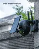 A black security camera with a solar panel attached, mounted on a stone wall in the rain. Produktbild-Vorschau