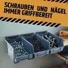 Three gray storage bins filled with screws and nails are mounted on a light gray wall. A yellow banner with black text is above the bins. Produktbild-Vorschau