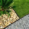 A close-up view of a garden border separating grass, large pebbles, and small gravel, with a palm plant visible. Produktbild-Vorschau