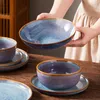 A person is holding a large blue and purple bowl over a wooden table with other dishes. Náhled obrázku produktu