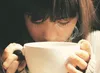 A person is holding a white mug and smelling the steam coming from it. Produktbild-Vorschau