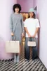 Two women stand in a hallway, each holding a handbag. Produktbild-Vorschau