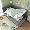 A child's bedroom with a grey corner daybed, featuring storage drawers, a green and white checkered comforter, and a green knitted throw. A colorful pillow and a bolster pillow are on the bed. A rug with a panda and a race track design is on the floor, wit Náhľad obrázku produktu