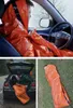 Collage of images showing an orange emergency bivvy bag being used in different scenarios: inside a car, being packed into a car trunk, and laid out on the ground. Podgląd zdjęcia produktu