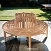 A circular wooden bench is placed on a wooden deck in a garden setting, with a lawn and trees in the background. Produktbild-Vorschau