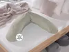 A V-shaped pillow is placed on a bed with a textured white bedspread. A knitted throw blanket is draped over the pillow and bed. Produktbild-Vorschau
