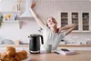A woman is stretching in a kitchen with a kettle and croissants on the counter. Náhled obrázku produktu