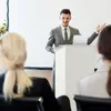 A man is giving a presentation at a podium to an audience. Anteprima dell’immagine prodotto