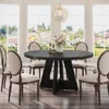 A dining room scene with a round black table and six beige chairs, set against large windows with a view of houses and greenery. Anteprima dell’immagine prodotto