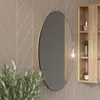 A round mirror with a wooden frame hangs on a wall with patterned wallpaper. A wooden shelf unit with toiletries is visible to the right, and a plant is in the foreground. Náhled obrázku produktu