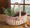 A wicker basket filled with flowers sits on a wooden surface, with a window showing a mountain landscape in the background. Produktbild-Vorschau