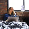 A woman is in bed using a laptop, with a humidifier on the windowsill. Voir les images du produit