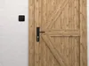 A wooden door with a black door handle and a black light switch on a textured wall. Produktbild-Vorschau