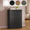 A dark gray chest of drawers is shown in a room with a light pink wall and wooden floor. There are decorative items on top of the dresser, and a sofa is visible in the background. Podgląd zdjęcia produktu