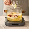 A person is adding a slice of pear to a glass pot filled with liquid and fruit, placed on a portable induction cooker. Produktbild-Vorschau