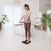 A woman is using a digital body analysis scale in a modern, well-lit bathroom. Produktbild-Vorschau