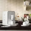 A white SMEG coffee machine is shown on a dark countertop, with coffee cups and a jar of coffee beans nearby. Voir les images du produit