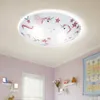 A close-up view of a ceiling light with unicorn and star decorations, mounted on a white ceiling above a pink-painted wall in a child's room. Shelves with decorative items are visible on the wall. Produktbild-Vorschau