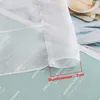 A close-up view of the hem of a white sheer curtain, showing stitching and a measurement indicator. Produktbild-Vorschau