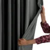 A person is holding open a dark gray curtain, revealing a black curtain behind it. Produktbild-Vorschau