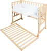 A wooden crib with bedding and a separate wooden slatted base, shown against a white background. Produktbild-Vorschau