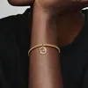 A close-up shot of a person's arm wearing a gold bracelet with a dangling charm. Podgląd zdjęcia produktu