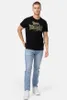A man wearing a black t-shirt and light blue jeans, standing against a white background. Produktbild-Vorschau