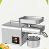A stainless steel automatic oil press machine is shown on a light gray and white background, with some peanuts in the lower left corner. Náhled obrázku produktu