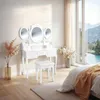 A white vanity table with a tri-fold mirror and a stool in a bedroom, next to a large window with a view of mountains and a river. Voir les images du produit