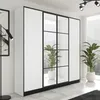 A modern white wardrobe with black framing and glass doors, set in a bright room with plants and a window view. Produktbild-Vorschau