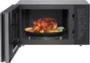 A whole roasted chicken with vegetables inside an open microwave. Produktbild-Vorschau