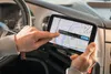 A person's hands are holding and interacting with a GPS navigation device inside a car. Voir les images du produit