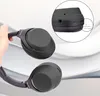 A hand holding a pair of black Sony headphones, with a close-up inset showing the side of the headphone ear cup with a measurement indicator. Produktbild-Vorschau