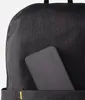 A close-up shot of a dark gray backpack with a black electronic device partially inserted into a front pocket. Náhled obrázku produktu