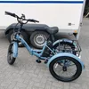 A blue electric tricycle is parked on a paved surface in front of a white trailer. Podgląd zdjęcia produktu
