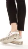Close-up of a person's feet wearing white sneakers with a grey sole and black pants. Podgląd zdjęcia produktu
