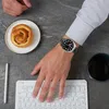 A person's hand with a watch on their wrist is typing on a keyboard, with a pastry and a cup of coffee nearby. Produktbild-Vorschau