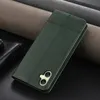 A dark green leather phone case is shown lying on a dark surface, with rolls of fabric in the background. Produktbild-Vorschau