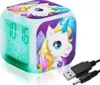 A cube-shaped digital alarm clock with a unicorn design, displaying the time, day, and temperature on its LCD screen. It is shown with a USB cable. Produktbild-Vorschau