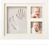 A baby handprint and footprint cast in a white wooden frame with two photos of a baby. Produktbild-Vorschau