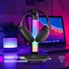 A gaming headset stand with RGB lighting and a wireless charger, placed on a desk with a laptop and a decorative lamp in the background. Produktbild-Vorschau