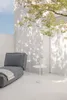An outdoor lounge chair with a small side table and watering can, set against a white wall with dappled sunlight from a tree. Podgląd zdjęcia produktu