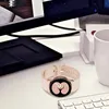 A smartwatch is placed on a desk next to a computer monitor and keyboard. Produktbild-Vorschau