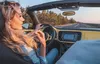 A woman driving a yellow convertible car on a road with trees on the side. Produktbild-Vorschau