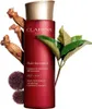 A red bottle of Clarins Super Restorative Smoothing Treatment Essence is displayed with natural elements like ginseng roots and leaves. Náhled obrázku produktu