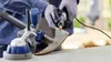 A person wearing gloves is using a Dremel tool to sharpen an axe that is held in a vise. Produktbild-Vorschau