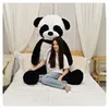 A young woman is sitting on a bed next to a very large stuffed panda bear. The room is decorated with fairy lights and draped curtains. Produktbild-Vorschau